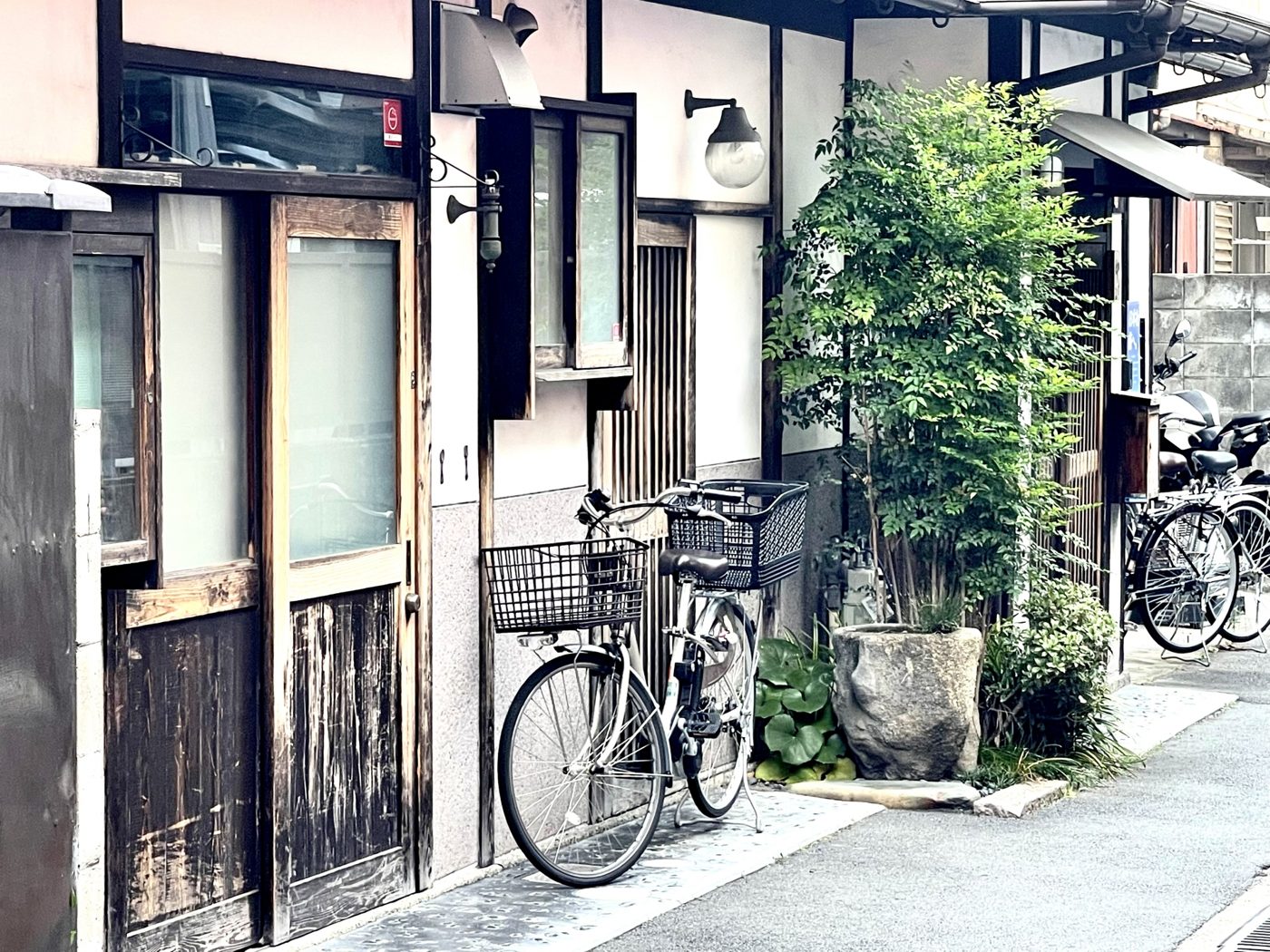 自転車と植木が並ぶ、古い家が軒を連ねる路地
