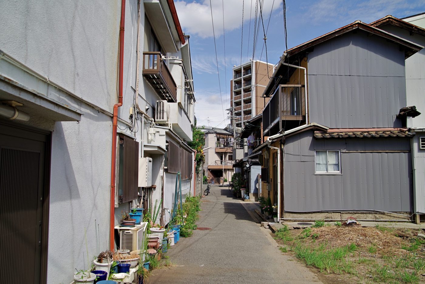 トタン張りの古い木造住宅と、奥にマンションが見える路地
