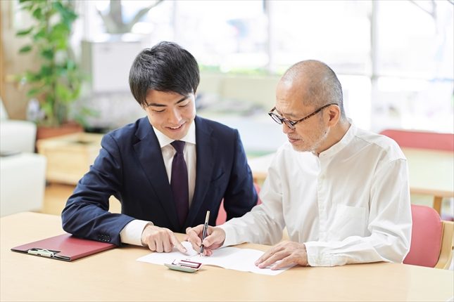 高齢の男性が担当者と書類を確認する様子